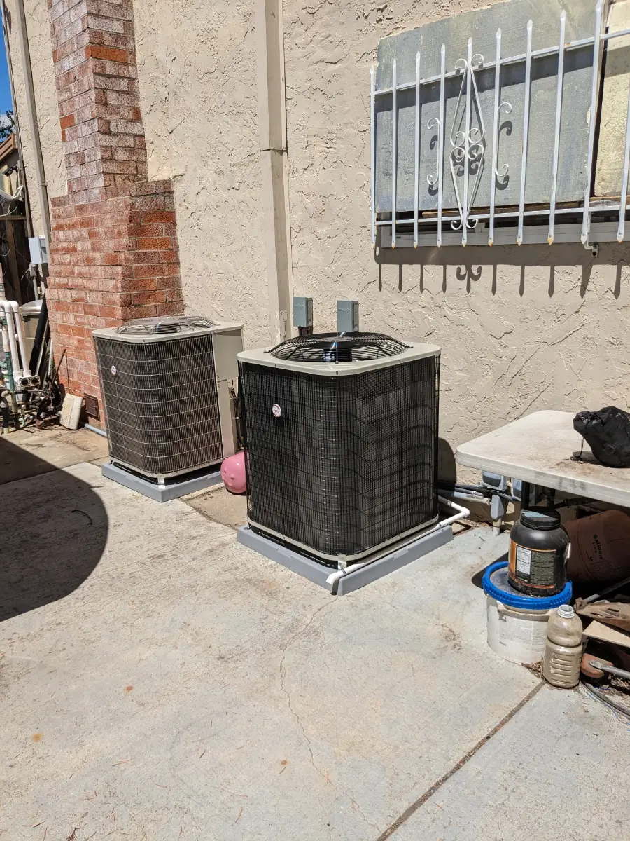 Two air conditioners are sitting outside on the patio.