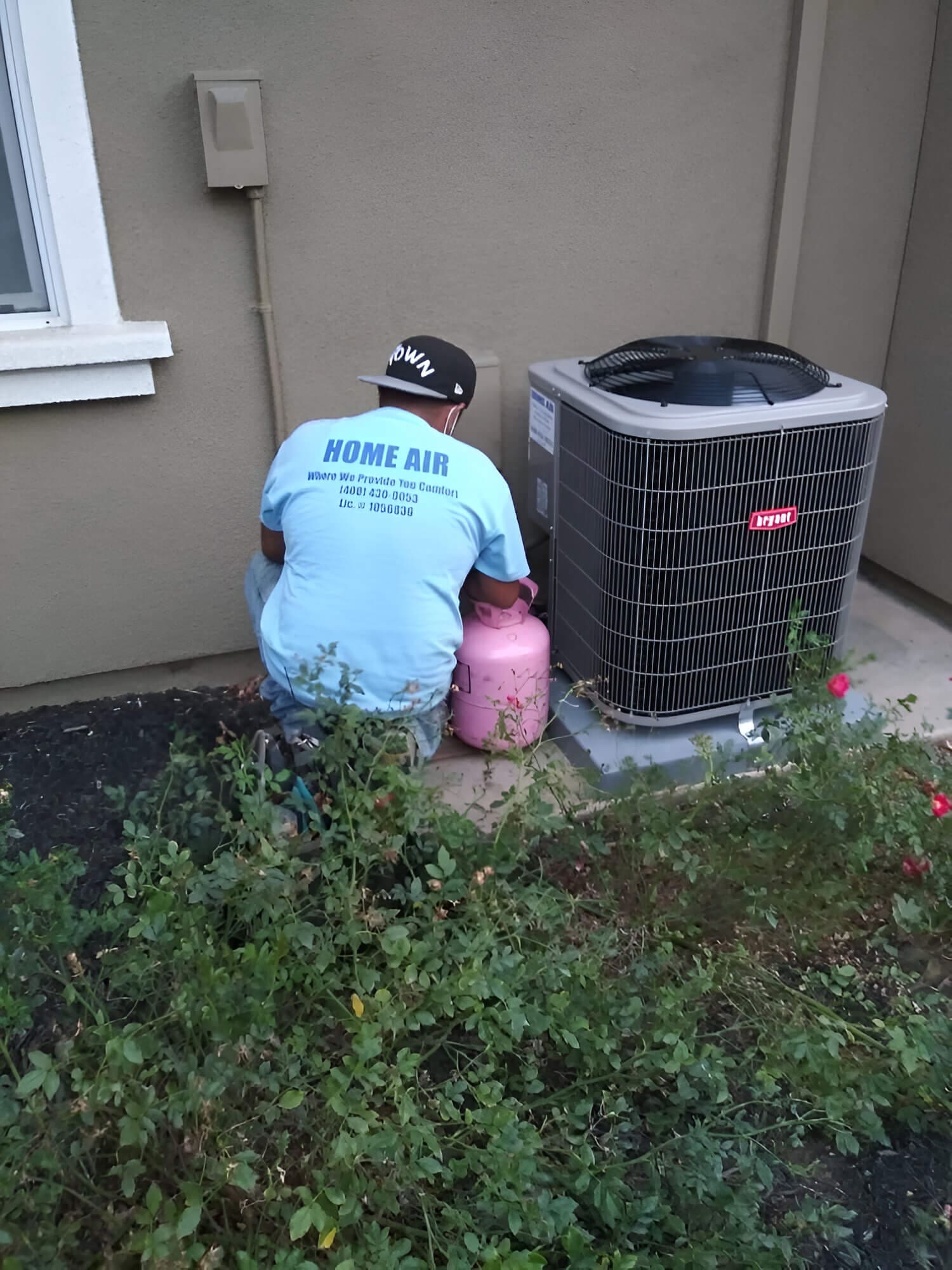 A man is sitting on the ground next to an air conditioner.